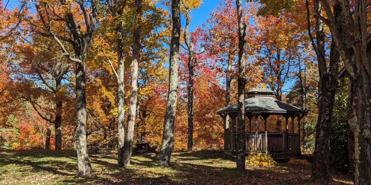 Wooden gazebo on the Love Ridge Mountain Lodging campus surrounded by peak fall foliage in orange red and gold under a bright blue sky.