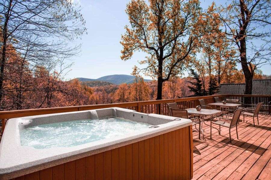 Large outdoor hot tub for seven guests on a private deck with table and chairs overlooking fall foliage and the Blue Ridge Mountains at Love Ridge Mountain Lodging.
