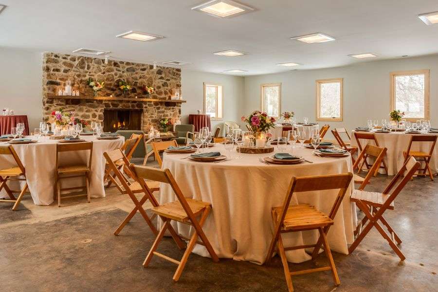 Elegant event setup inside the Love Ridge Lodge with round tables, floral centerpieces, and a stone fireplace: ideal for weddings, holiday dinners, and group celebrations in the Blue Ridge Mountains.